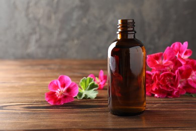 Photo of Geranium essential oil in bottle and beautiful flowers on wooden table