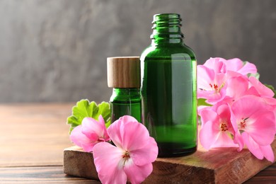 Geranium essential oil in bottles and beautiful flowers on wooden table