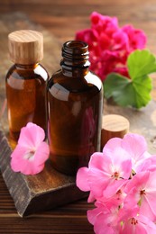 Photo of Geranium essential oil in bottles and beautiful flowers on wooden table