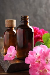 Photo of Geranium essential oil in bottles and beautiful flowers on wooden table