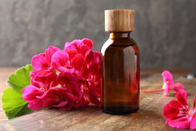 Photo of Geranium essential oil in bottle and beautiful flowers on wooden table