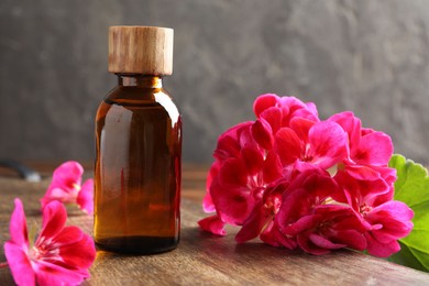 Photo of Geranium essential oil in bottle and beautiful flowers on wooden table