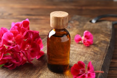 Photo of Geranium essential oil in bottle and beautiful flowers on wooden table