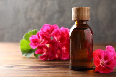 Photo of Geranium essential oil in bottle and beautiful flowers on wooden table