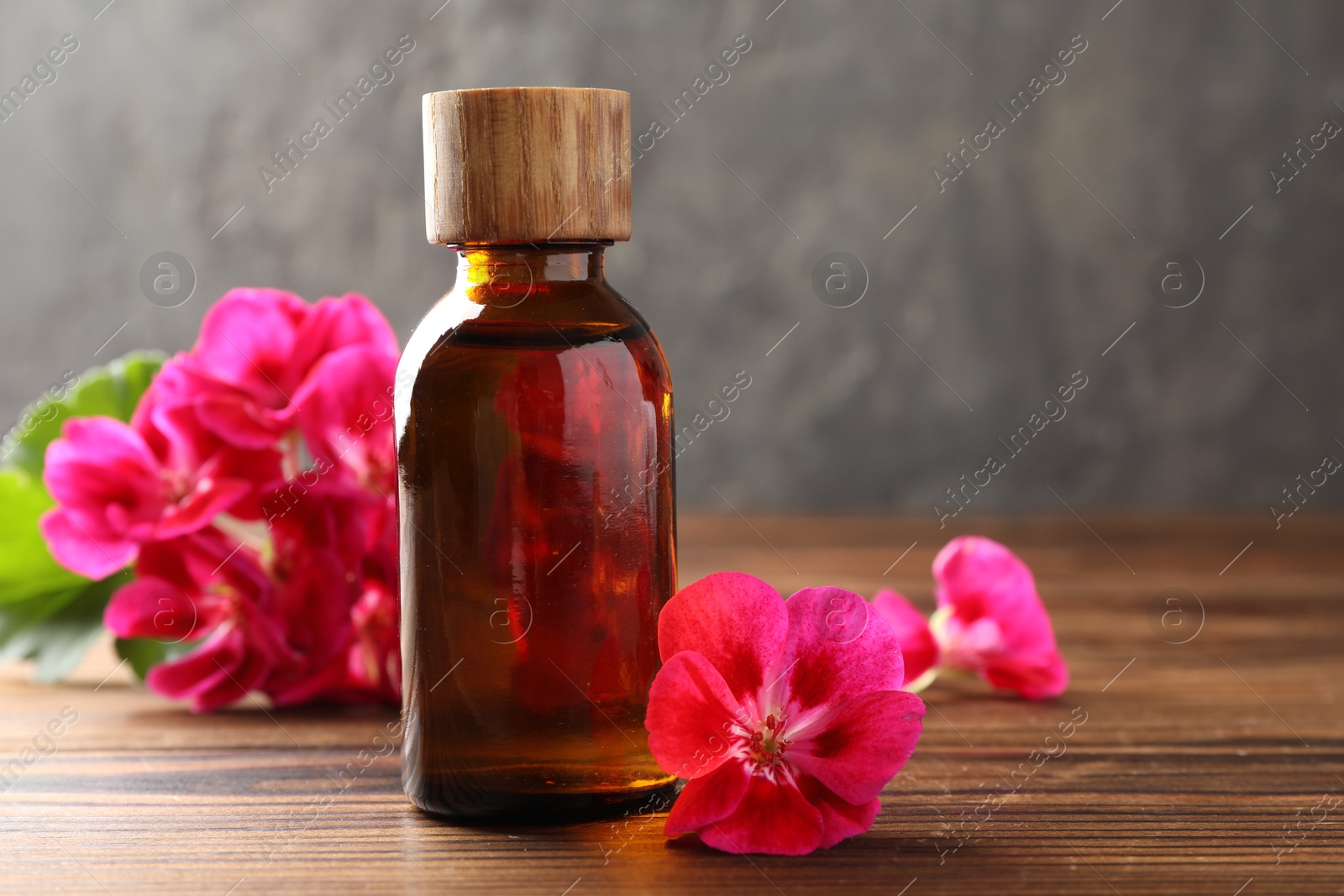 Photo of Geranium essential oil in bottle and beautiful flowers on wooden table