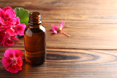 Photo of Geranium essential oil in bottle and beautiful flowers on wooden table, space for text