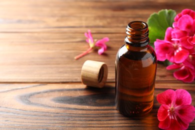 Photo of Geranium essential oil in bottle and beautiful flowers on wooden table, space for text