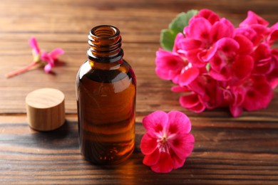 Photo of Geranium essential oil in bottle and beautiful flowers on wooden table