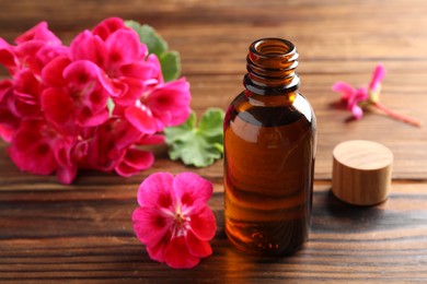 Photo of Geranium essential oil in bottle and beautiful flowers on wooden table