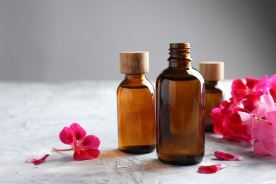 Photo of Bottles of geranium essential oil and beautiful flowers on light grey textured table, closeup