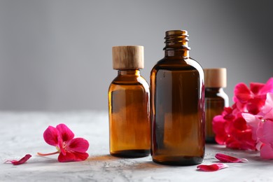 Photo of Bottles of geranium essential oil and beautiful flowers on light grey textured table, closeup