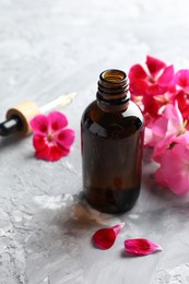 Photo of Bottle of geranium essential oil and beautiful flowers on light grey textured table