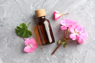 Photo of Bottle of geranium essential oil and beautiful flowers on light grey textured table, flat lay