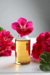 Photo of Bottle of geranium essential oil and beautiful flowers on white wooden table