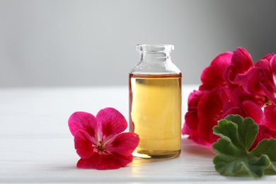 Photo of Bottle of geranium essential oil and beautiful flowers on white wooden table, closeup