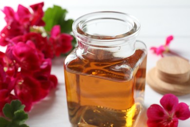 Photo of Bottle of geranium essential oil and beautiful flowers on white table, closeup