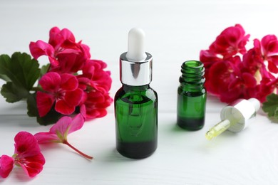 Photo of Geranium essential oil, pipette and beautiful flowers on white wooden table, closeup