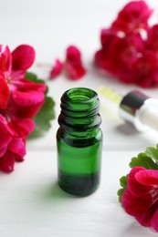 Photo of Bottle of geranium essential oil and beautiful flowers on white wooden table, closeup