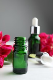 Photo of Bottles of geranium essential oil and beautiful flowers on white wooden table, closeup