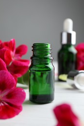 Photo of Bottles of geranium essential oil and beautiful flowers on white wooden table, closeup