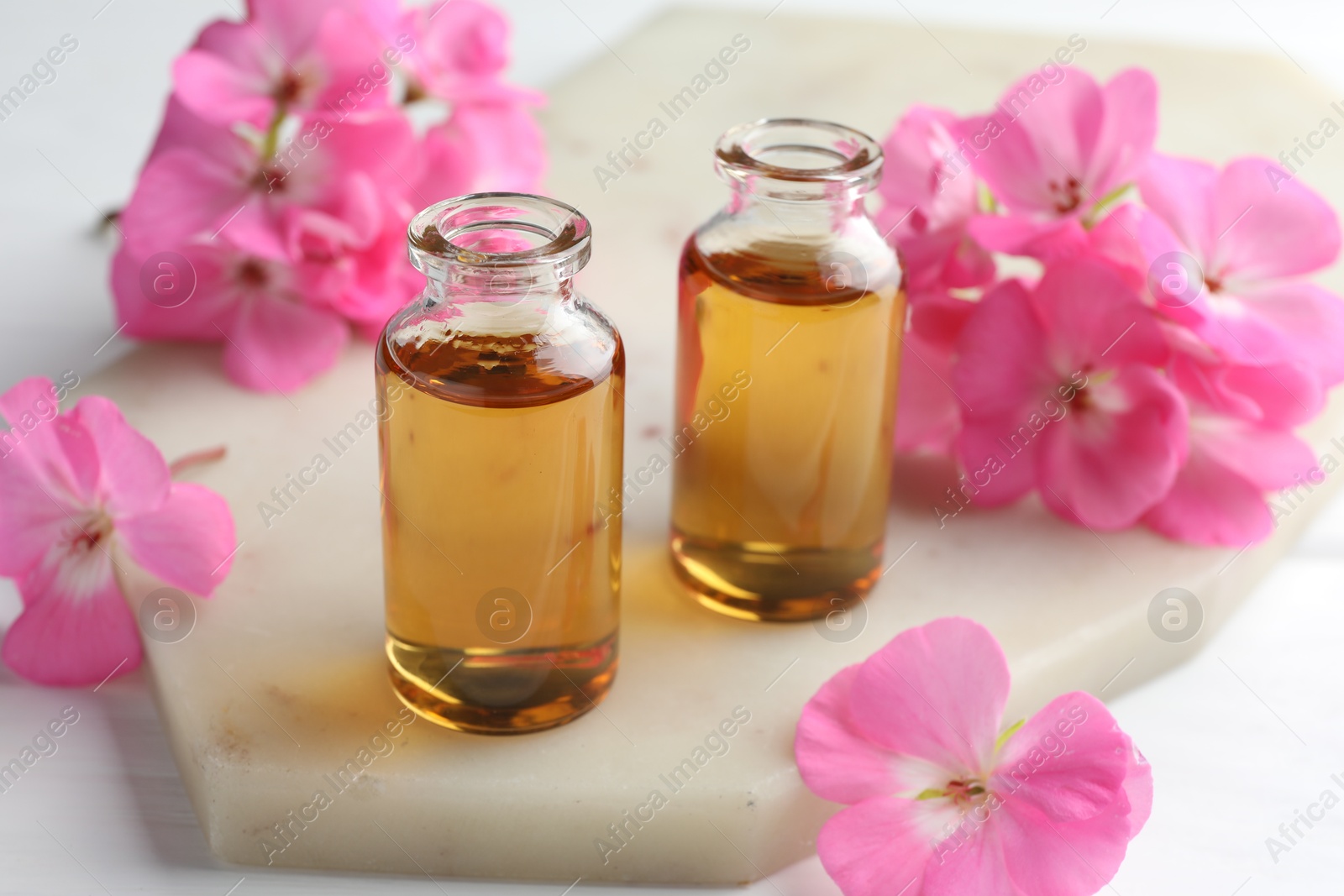 Photo of Bottles of geranium essential oil and beautiful flowers on white table, closeup