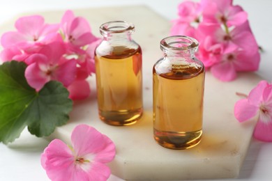 Photo of Bottles of geranium essential oil and beautiful flowers on white table, closeup