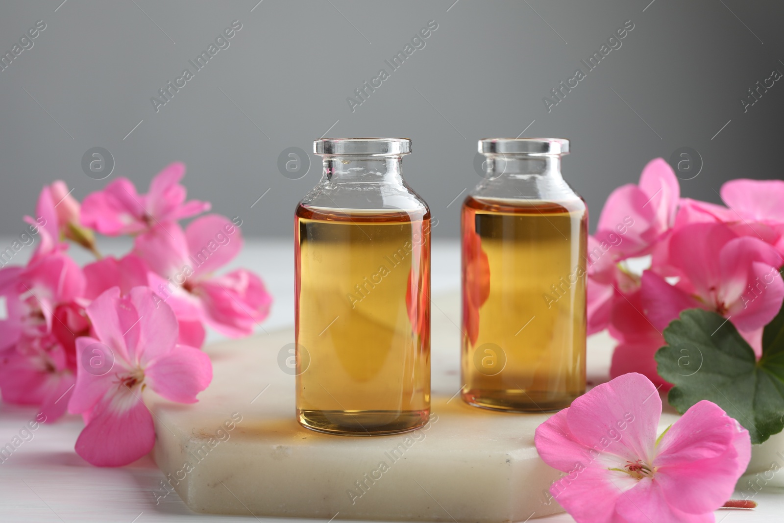 Photo of Bottles of geranium essential oil and beautiful flowers on white table, closeup