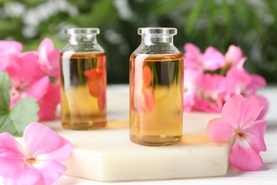 Photo of Bottles of geranium essential oil and beautiful flowers on white table, closeup