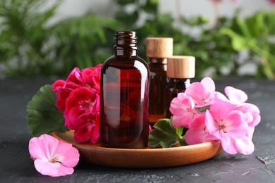 Photo of Bottles of geranium essential oil and beautiful flowers on black table, closeup