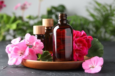 Photo of Bottles of geranium essential oil and beautiful flowers on black table, closeup