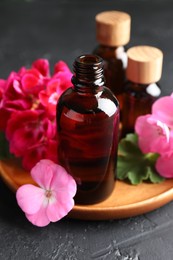 Photo of Bottles of geranium essential oil and beautiful flowers on black table, closeup