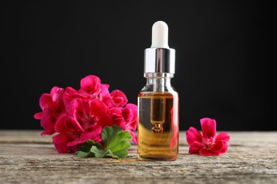 Photo of Bottle of geranium essential oil and beautiful flowers on wooden table, closeup