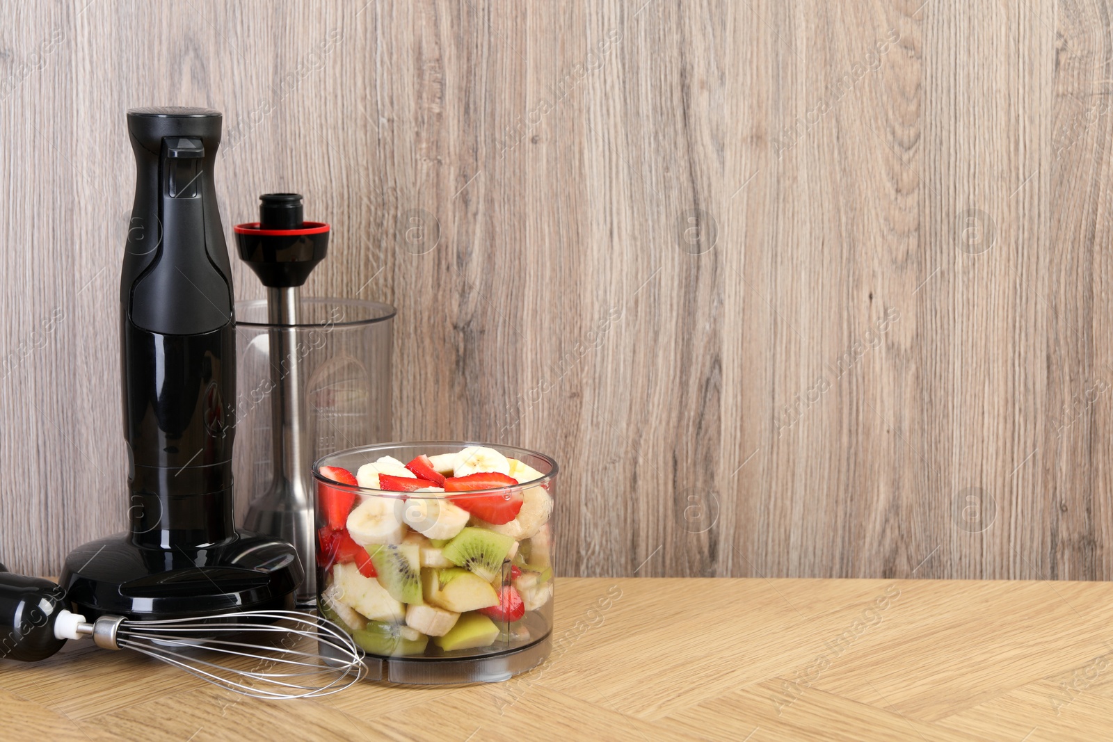 Photo of Hand blender kit with fresh fruits and strawberries on wooden table, space for text