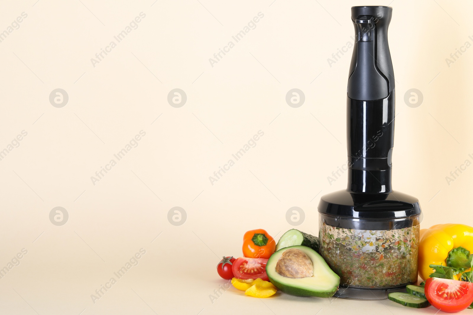 Photo of Hand blender with mixture of ingredients and fresh products on beige background, space for text