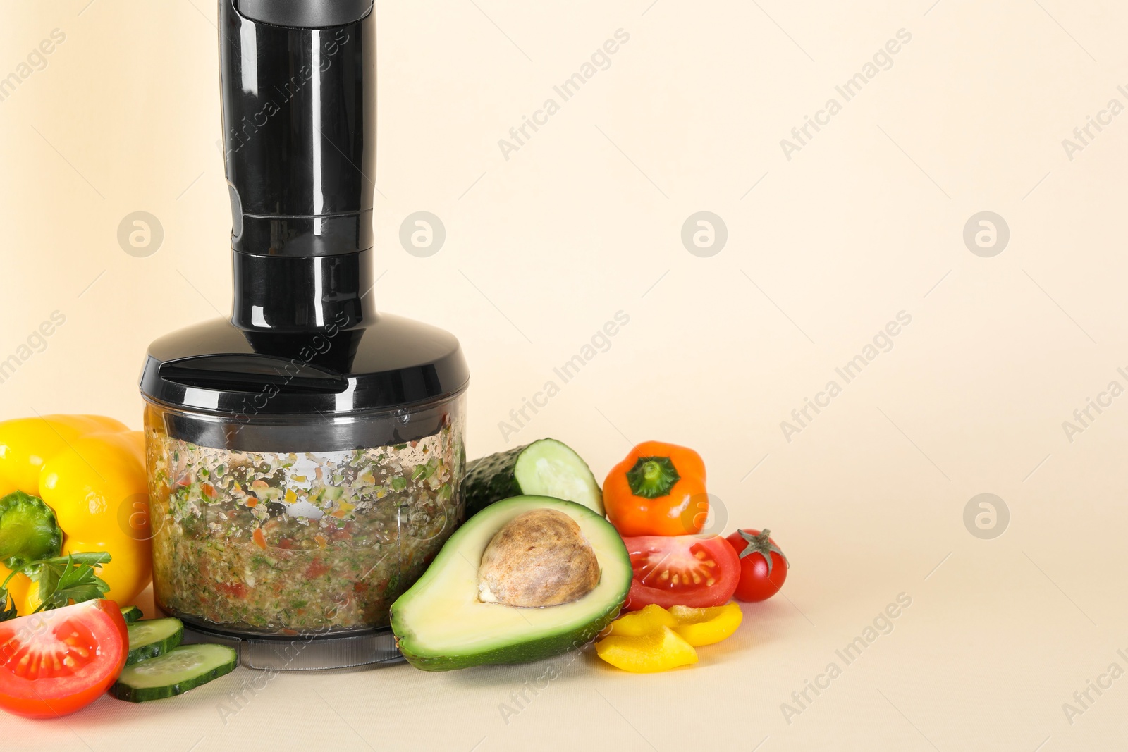 Photo of Hand blender with mixture of ingredients and fresh products on beige background, space for text