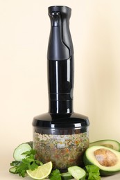 Photo of Hand blender with mixture of ingredients and fresh products on beige background