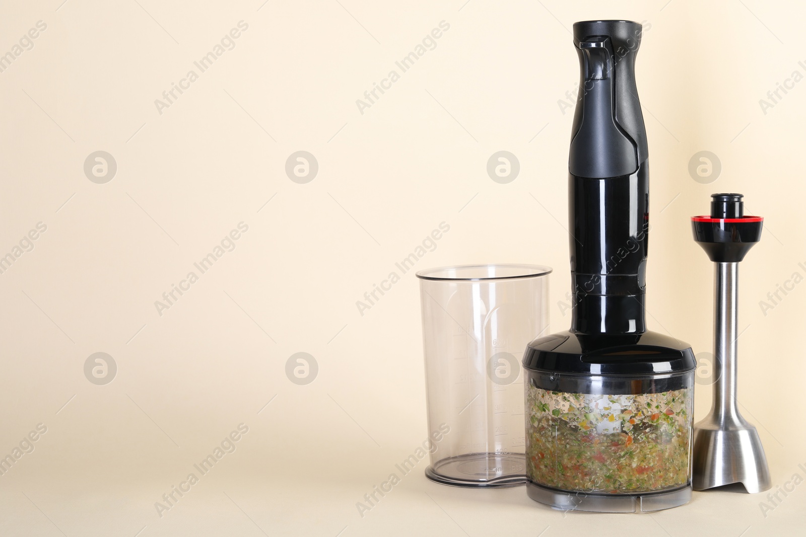 Photo of Hand blender kit and mixture of ingredients on beige background, space for text