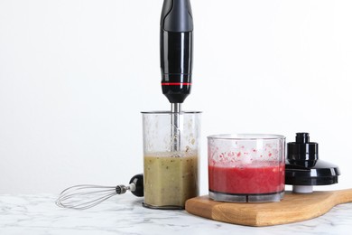 Photo of Hand blender kit and mixtures of ingredients on white marble table