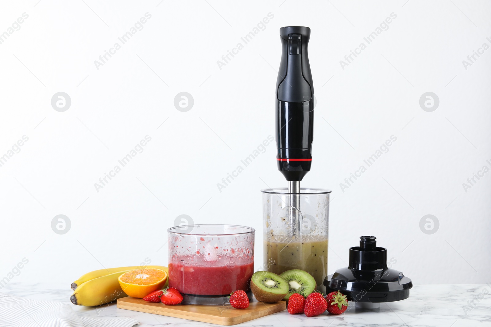 Photo of Hand blender kit, mixtures of ingredients and fresh fruits on white marble table