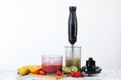 Hand blender kit, mixtures of ingredients and fresh fruits on white marble table