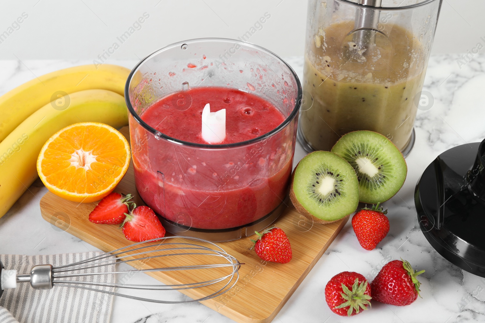 Photo of Hand blender kit, mixtures of ingredients and fresh fruits on white marble table