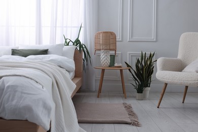 Stylish living room interior with bed, bedside table, lamp and houseplants