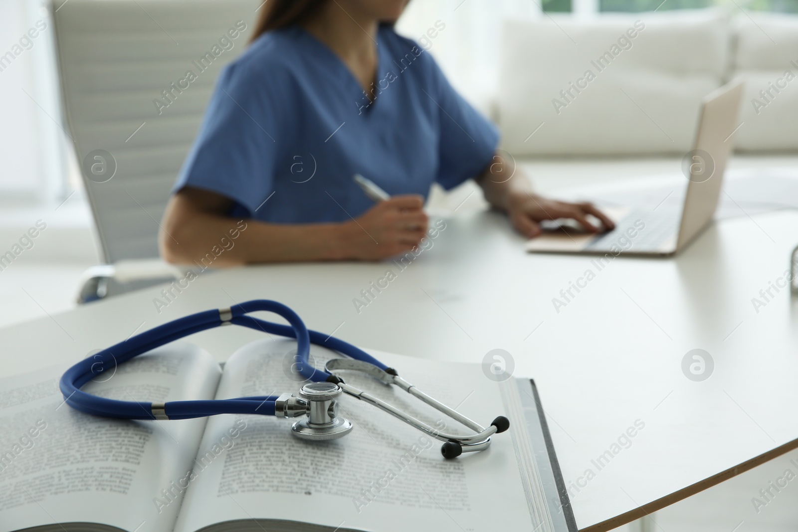 Photo of Doctor at white table in hospital, focus on medical stethoscope and book