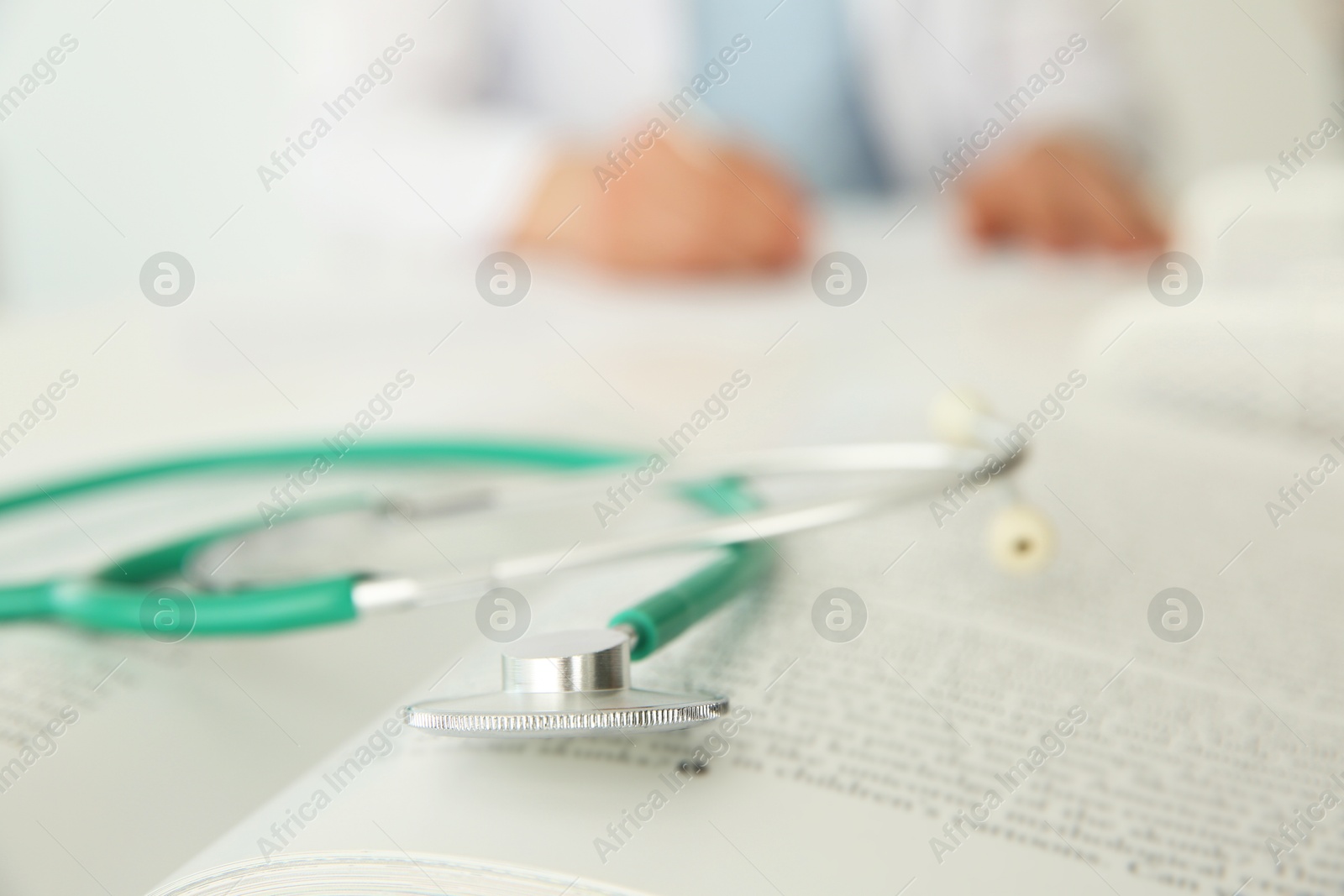 Photo of Doctor at table in hospital, focus on medical stethoscope and book