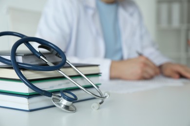 Photo of Doctor at white table in hospital, focus on medical stethoscope and books