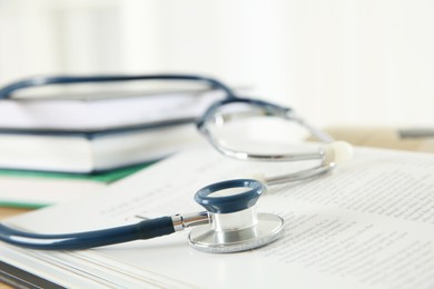 Photo of One new medical stethoscope and books on table, closeup