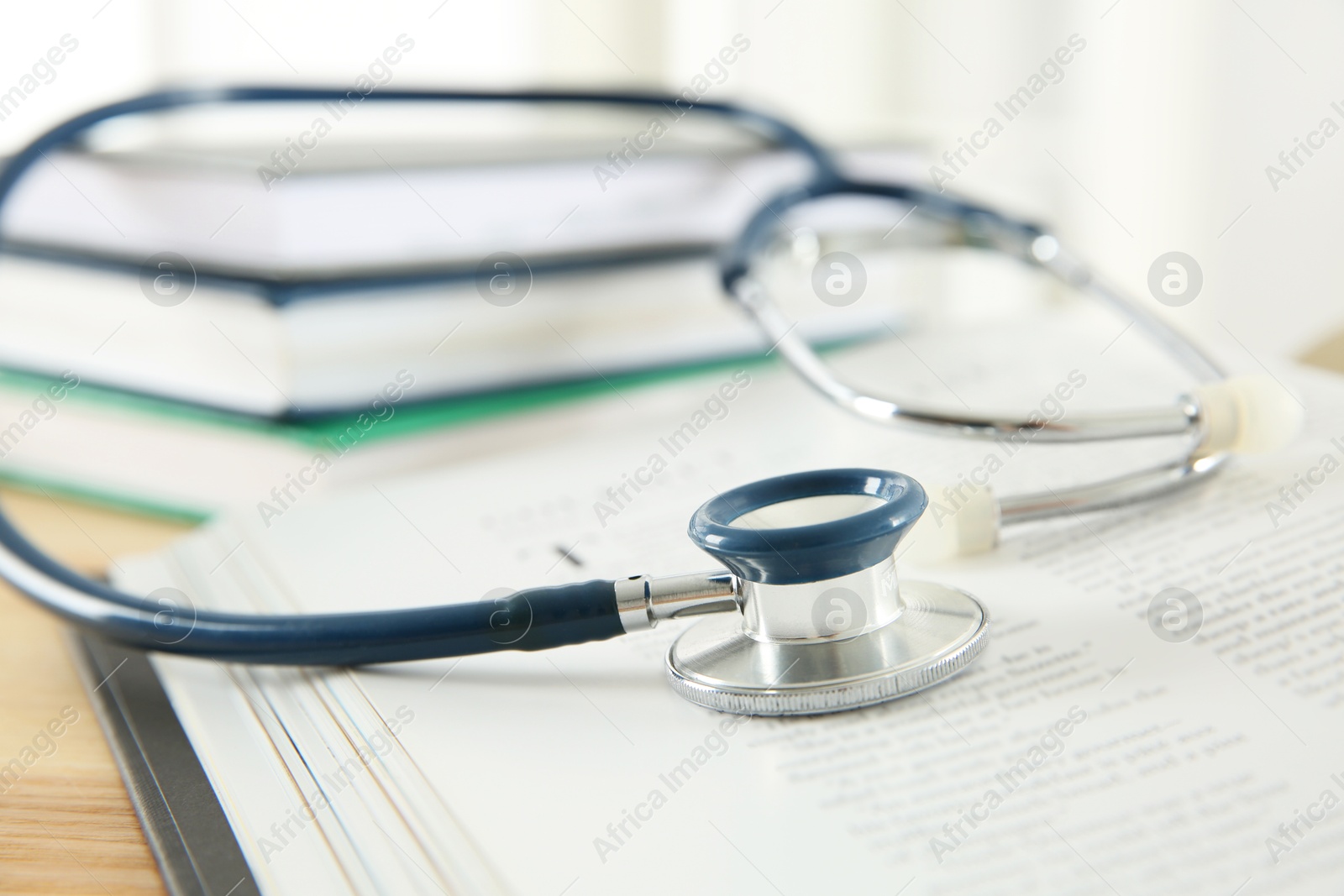 Photo of One new medical stethoscope and books on wooden table, closeup