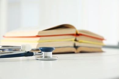 One new medical stethoscope and books on white wooden table, closeup