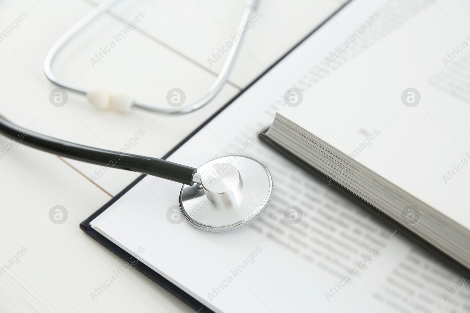 Photo of One new medical stethoscope and books on white wooden table, closeup