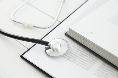 One new medical stethoscope and books on white wooden table, closeup